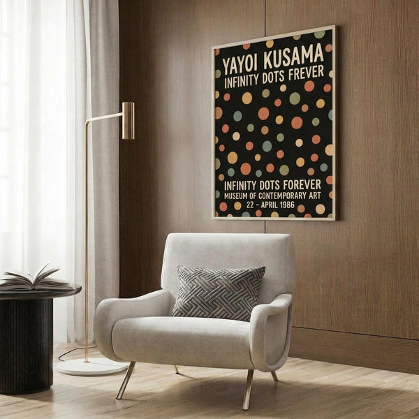 May include: Framed exhibition poster featuring colorful polka dots on black background displayed on wood paneled wall above beige armchair with geometric throw pillow, brass floor lamp and side table with open book nearby, warm neutral modern interior setting