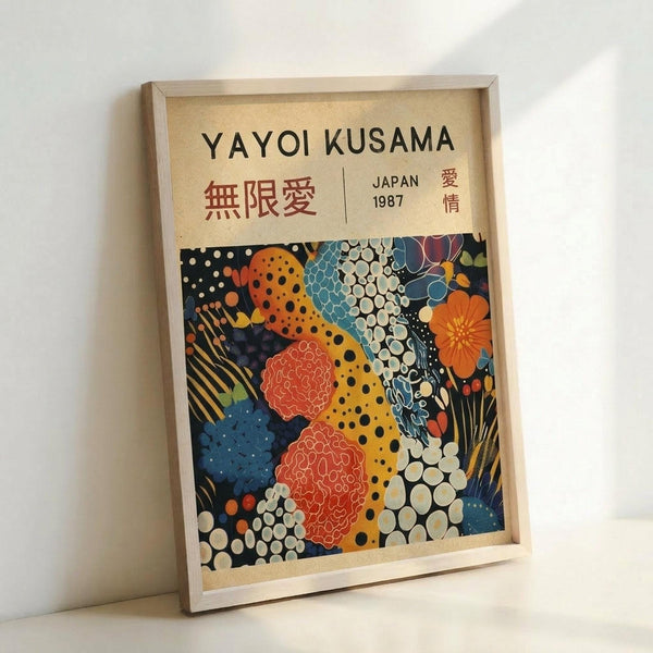 May include: Framed poster print leaning against white wall corner featuring colorful abstract pattern with organic shapes, polka dots, and cellular forms in orange, blue, red, and yellow against dark background. Light wood frame surrounds cream-colored mat with "YAYOI KUSAMA" text and Japanese characters at top, plus "JAPAN 1987" marking. Artwork displays vibrant, psychedelic style with flowing, interconnected forms and varied textures.