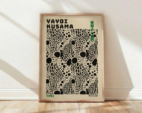 May include: Framed poster with black polka dot pattern on cream background, displayed against white textured wall on light wood floor. Features "YAYOI KUSAMA" text at top, Japanese characters in green, and "1992" date marking. The artwork shows flowing organic dots in various sizes creating an infinity net design. Natural wood frame complements the minimalist room setting with soft window light creating gentle shadows.