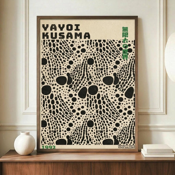 May include: Framed poster with black polka dot pattern on cream background, featuring "YAYOI KUSAMA" text and green Japanese characters, displayed on wooden sideboard next to white ceramic vase and stacked books in elegant room with white paneled walls