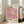 May include: Framed poster with colorful polka dot pattern in pink, purple, orange and cream tones, featuring "YAYOI KUSAMA" text and Japanese characters. Light wood frame leaning against white wall next to beige upholstered chair in bright, airy room with large windows and natural sunlight streaming across hardwood floors.