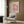 May include: Colorful abstract art poster with pink, purple, and orange polka dots on cream background, displayed in modern living room with beige armchair, geometric throw pillow, brass floor lamp, and wood paneled wall. Japanese text visible on vintage-style exhibition poster in light wooden frame.