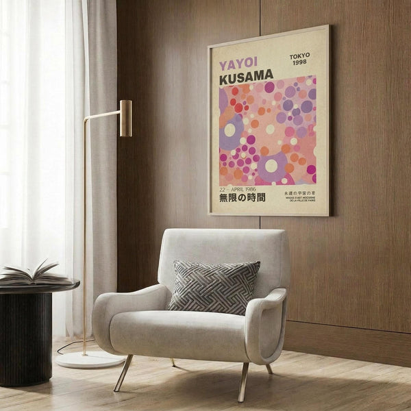 May include: Colorful abstract art poster with pink, purple, and orange polka dots on cream background, displayed in modern living room with beige armchair, geometric throw pillow, brass floor lamp, and wood paneled wall. Japanese text visible on vintage-style exhibition poster in light wooden frame.