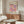 May include: Colorful polka dot art poster in thin frame hanging above wooden credenza in modern living room. Artwork features purple, pink, orange and white circles on cream background with "YAYOI KUSAMA" and "TOKYO 1998" text. Room has white curved chair, glass oval coffee table, floor lamp, and neutral walls with natural lighting.