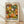 May include: Framed poster with colorful abstract floral pattern featuring overlapping circular and daisy-like shapes in orange, green, yellow, white, and black dots. The artwork displays "YAYOI KUSAMA" and Japanese text with "NAGOYA" below. Light wood frame sits on wooden floor against white textured wall with soft natural lighting creating gentle shadows.