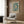 May include: Framed poster with blue and cream jellyfish pattern artwork hanging on wood paneled wall above beige upholstered armchair with geometric pillow. Modern brass floor lamp and black side table with open book visible. Neutral toned room setting with natural lighting from window.