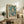 May include: Framed poster with turquoise blue jellyfish pattern featuring cream and white floating jellyfish with flowing tentacles, displayed on rustic wooden sideboard alongside fern plant, ceramic vase, and stacked books in neutral-toned living room with beige armchair and white walls