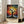 May include: Framed art print leaning against white wall next to beige sofa in bright room with large windows. The poster features a vibrant tree with black silhouette trunk and branches, surrounded by colorful dots in rainbow hues of red, orange, yellow, green, blue creating a dreamy, cosmic atmosphere. Text appears below the artwork in both English and Japanese characters. Natural lighting creates soft shadows on hardwood flooring.