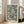 May include: Framed poster with turquoise and cream jellyfish illustration leaning against white wall next to beige sofa in bright living room. Artwork shows floating jellyfish with trailing tentacles against blue-green background, black text at bottom reading "YAYOI KUSAMA" and Japanese characters, "KYOTO" in corner. Light wood frame, natural lighting from tall windows.