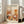 May include: Framed poster print featuring abstract botanical illustration in warm orange, terracotta, and cream tones with stylized plants, flowers, and geometric patterns. Text reads "YAYOI KUSAMA" with Japanese characters and "JAPAN 1987". Light wood frame displayed on floor against white wall beside beige sofa in bright, minimalist living room with large windows.