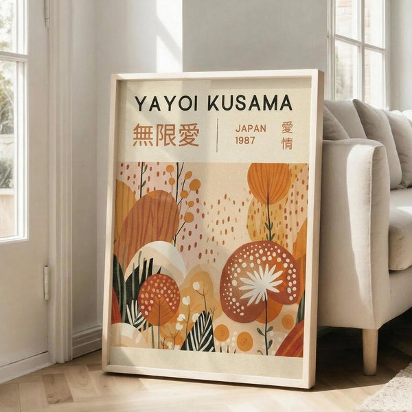 May include: Framed poster print featuring abstract botanical illustration in warm orange, terracotta, and cream tones with stylized plants, flowers, and geometric patterns. Text reads "YAYOI KUSAMA" with Japanese characters and "JAPAN 1987". Light wood frame displayed on floor against white wall beside beige sofa in bright, minimalist living room with large windows.