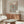 May include: Framed Yayoi Kusama exhibition poster with black polka dot pattern and red accents displayed on wooden sideboard in modern living room. Shows cream-colored furniture, glass coffee table, floor lamp, and neutral wall colors. Poster features spiral dot design with Japanese text and museum information.