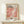 May include: Framed exhibition poster for Yayoi Kusama featuring pink and coral polka dot pattern artwork, displayed on light wood console table with small white gift box, against cream wall. Wood frame complements minimalist styling.