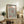 May include: Framed art print displayed on rustic wooden sideboard in neutral living room setting. Poster features black polka dot pattern on cream background with red circular elements and "YAYOI KUSAMA" text at top, referencing Musée d'Art Moderne de la Ville de Paris. Scene includes fern plant, ceramic vase, books, and beige upholstered chair with brown leather cushion.