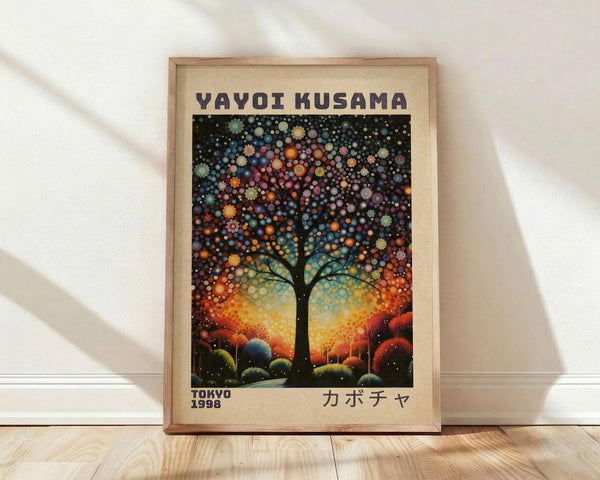May include: Framed art print leaning against white wall on light wood floor. Features a silhouetted tree with spreading branches against a cosmic background of colorful dotted circles in blues, oranges, purples, and yellows. The tree sits on rolling hills beneath a starry sky. Text reads "YAYOI KUSAMA" at top, "TOKYO 1998" at bottom left, and Japanese characters at bottom right. Natural wood frame with cream matting.