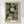 May include: Framed art print hanging on white wall featuring stylized dandelion-like flowers with dotted circular patterns in cream and white against dark green background. Brown stems connect the blooms. Japanese text appears at bottom with "YAYOI KUSAMA" and "KYOTO" in bold black letters. Light wood frame surrounds the vintage-style botanical poster design with pointillistic dot technique throughout.