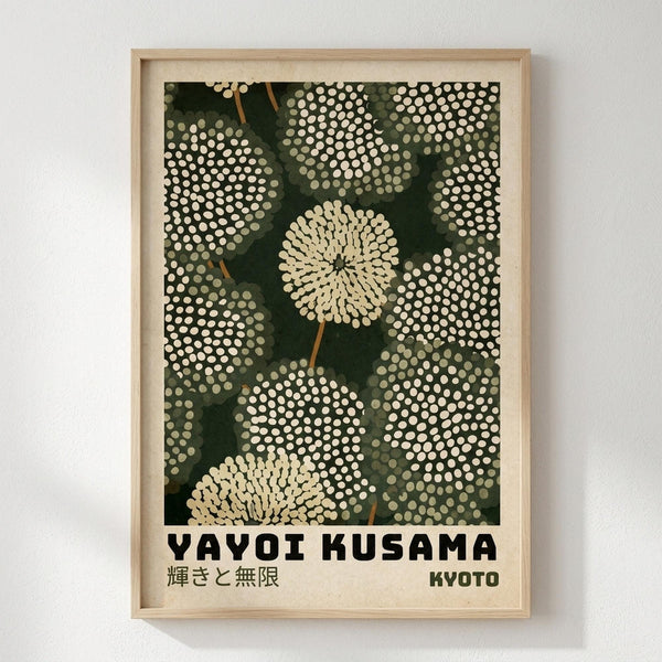 May include: Framed art print hanging on white wall featuring stylized dandelion-like flowers with dotted circular patterns in cream and white against dark green background. Brown stems connect the blooms. Japanese text appears at bottom with "YAYOI KUSAMA" and "KYOTO" in bold black letters. Light wood frame surrounds the vintage-style botanical poster design with pointillistic dot technique throughout.