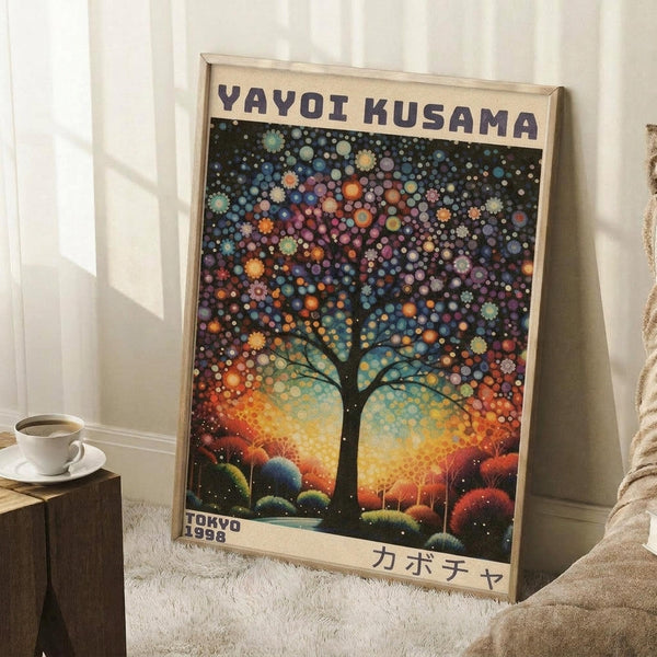 May include: Framed poster featuring a silhouetted tree with colorful polka dot foliage against a vibrant sunset sky, displaying "YAYOI KUSAMA" at top and "TOKYO 1998" at bottom with Japanese characters. The artwork shows Kusama's signature dot style in blues, oranges, purples, and yellows. Frame leans against white paneled wall next to wooden side table with coffee cup, positioned on white textured rug beside beige upholstered furniture.