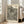 May include: Framed art print leaning against white wall next to beige upholstered chair in bright living room. Poster features black polka dots of varying sizes on cream background with wavy striped pattern cutting diagonally through center. Bold black text at top reads artist name, location and year. Museum attribution at bottom. Light wood frame, natural lighting from large windows.