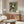 May include: Modern living room mockup showing framed poster with green background and white dotted circular patterns resembling chrysanthemums or dandelions, with Japanese text at bottom. Poster displayed above mid-century walnut credenza alongside brass floor lamp and table lamp. White curved chair and glass oval coffee table complete the minimalist Scandinavian-inspired interior scene.
