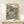 May include: Framed museum exhibition poster featuring Yayoi Kusama's signature black polka dot pattern on cream background, displayed on light wood console table against white wall. Small wrapped gift box with greenery sits beside the thin wooden frame.
