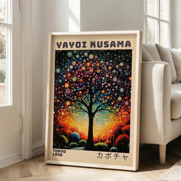 May include: Framed poster leaning against white wall next to beige sofa in bright living room. Artwork features colorful dotted tree with vibrant polka dot canopy in blues, oranges, and purples against cosmic background. Text reads "YAYOI KUSAMA" at top and "TOKYO 1998" at bottom with Japanese characters. Light wood frame on hardwood floor near large windows.