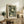 May include: Framed poster with green background and white polka dot pattern resembling dandelion seed heads, displayed on rustic wooden sideboard alongside fern plant, books, and ceramic vase in neutral-toned living room setting with cream armchair visible.