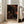 May include: Framed poster with black background featuring scattered circles and dots in orange, rust, and cream tones arranged in cosmic pattern, with "YAYOI KUSAMA" and Japanese text at bottom. Light wood frame leaning against white wall next to beige upholstered chair in bright room with large windows.