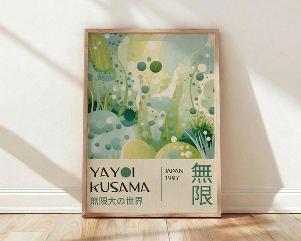 May include: Framed art print leaning against white wall on light wood floor with natural sunlight casting shadows. Abstract botanical artwork features overlapping green circles, dots, and leaf shapes in various shades of sage, teal, and yellow-green. Text reads "YAYOI KUSAMA" with Japanese characters and "JAPAN 1987" below the dreamy, organic composition in thin wood frame.