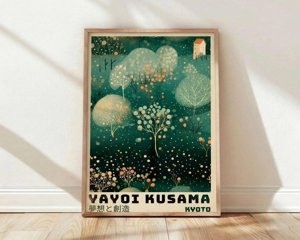 May include: Framed poster with stylized Japanese-inspired artwork featuring emerald green background dotted with cream and orange circles resembling falling snow or lights. Abstract trees and foliage in various shades of green fill the composition, with a small house visible in upper right corner. Bold black text reads "YAYOI KUSAMA" with Japanese characters below and "KYOTO" in bottom right. Light wood frame rests against white wall on wooden floor with soft shadows.