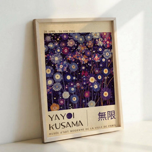 May include: Framed museum exhibition poster featuring Yayoi Kusama's colorful floral artwork on dark purple background with scattered daisy-like flowers in blues, oranges, and pinks. Text shows dates "28. APRIL - 14. MAI 1984" and "MUSÉE D'ART MODERNE DE LA VILLE DE PARIS" on cream colored background. Light wood frame leans against white wall.