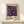 May include: Framed vintage exhibition poster with dark purple background featuring colorful abstract flowers and circles in blues, pinks, and yellows. Text reads "YAYOI KUSAMA" and shows museum details. Natural wood frame sits on light wooden console table next to small wrapped white gift box with pine sprig against cream wall.