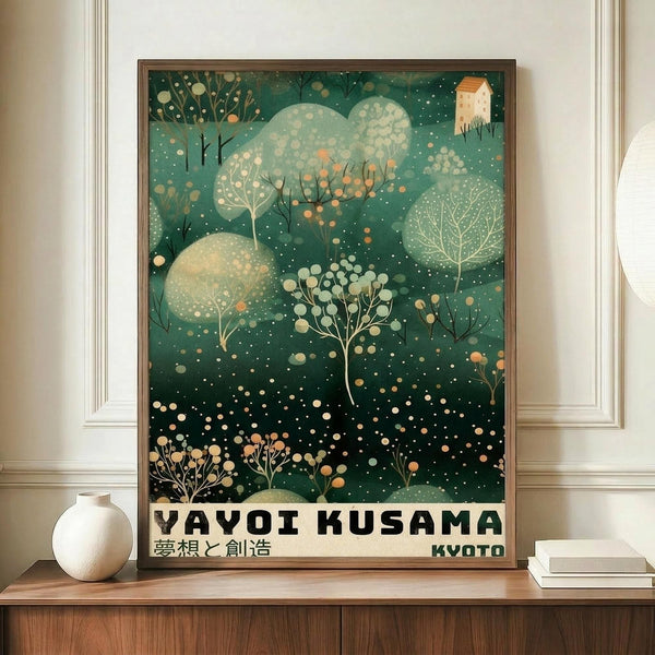 May include: Framed poster with green background featuring stylized trees, polka dots, and a small house in artistic style reminiscent of Kusama's work. The print displays "YAYOI KUSAMA" and "KYOTO" text at bottom with Japanese characters. Poster sits on wooden sideboard next to white ceramic vase and stacked books in modern interior with white walls and trim.