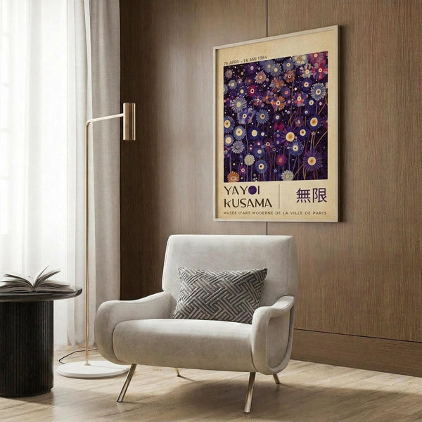 May include: Beige framed poster with purple background featuring colorful floral and circular patterns in blue, pink, and gold tones, displayed on wood paneled wall above light gray upholstered armchair with geometric patterned pillow, next to brass floor lamp and dark round side table with open book