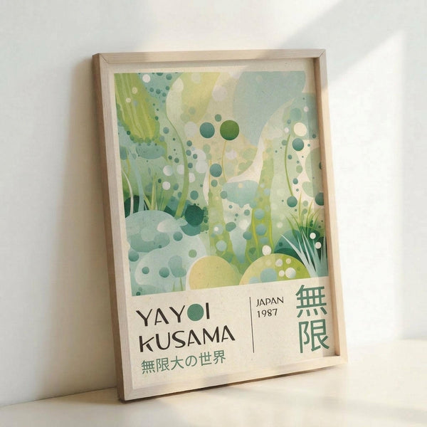 May include: Framed art print leaning against white wall featuring abstract botanical design in soft greens, blues, and yellows with polka dots and organic plant forms. Text reads "YAYOI KUSAMA" with Japanese characters and "JAPAN 1987" in minimal typography. Light wooden frame with natural finish, photographed in bright natural lighting showing subtle shadows.