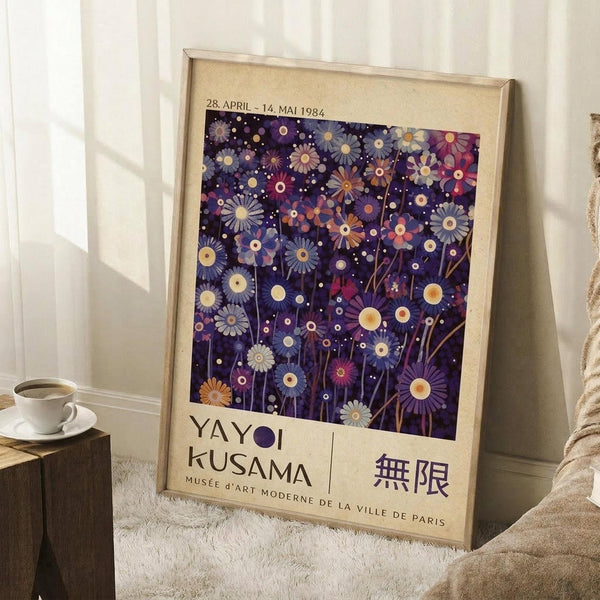 May include: Framed art print leaning against white wall corner on fluffy white rug. Features purple night sky filled with colorful daisy-like flowers in blues, purples, pinks, and yellows with white dots resembling stars. Text shows dates "28. APRIL - 14. MAI 1984" and "YAYOI KUSAMA MUSÉE D'ART MODERNE DE LA VILLE DE PARIS" with Japanese characters. Natural wood frame, cream matting. Small wooden stool with white coffee cup visible on left side.