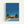May include: Framed art print in light wood frame hanging on white wall, featuring retro-style illustration of mid-century modern building with "PROUD" text, bright blue swimming pool in foreground, tall palm trees, vivid blue sky, and tropical landscaping in saturated colors reminiscent of 1980s aesthetic