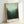 May include: Framed poster print leaning against white wall showing misty forest landscape in green gradient tones from dark forest silhouettes at bottom to pale mint sky above, with light wood frame and white border containing black text reading "MARK ROTHKO" and museum exhibition details