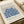 May include: Framed art print featuring blue coral-like botanical forms on beige background. White matted frame sits on neutral surface next to rolled cream paper and ribbon. Gallery-style poster with "MATISSE" at top, "BERGGRUEN & CIE" below artwork, includes Paris address and 1953 exhibition dates in French. Minimalist styling with warm lighting creates elegant display scene.