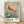 May include: Framed vintage Japanese art poster featuring golden-red koi fish swimming among delicate cherry blossoms in soft blue-green water. Exhibition poster shows "Ohara Shoson" text and Tokyo museum details from 1972. Natural wood frame displayed against white wall with soft shadows on light wooden floor.