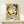 May include: Framed Henri Matisse exhibition poster with yellow background featuring abstract black silhouettes of two faces in profile, blue text in French mentioning paintings, drawings and sculptures. Wooden frame displayed on light wood shelf next to small wrapped white gift box with natural twine and dried plant sprig against cream wall.