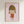 May include: Framed art print showing a cartoon-style illustration of a young girl with brown bob haircut, closed eyes, and tongue sticking out, wearing an orange-red dress. The character is drawn in a simple, minimalist style against a soft pink background. The artwork is displayed in a light wooden frame hanging on a white wall.
