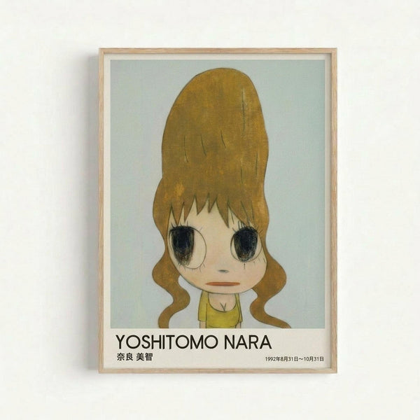 Framed art print featuring a cartoon-style illustration of a young girl with large golden-brown hair styled in an updo with curly tendrils. She has oversized dark eyes, pale skin, and wears a yellow top. The artwork has a soft, muted color palette against a light blue-green background. Below the image is text reading "YOSHITOMO NARA" with Japanese characters and dates "1992年8月31日～10月31日". The print is displayed in a light wooden frame against a white wall.