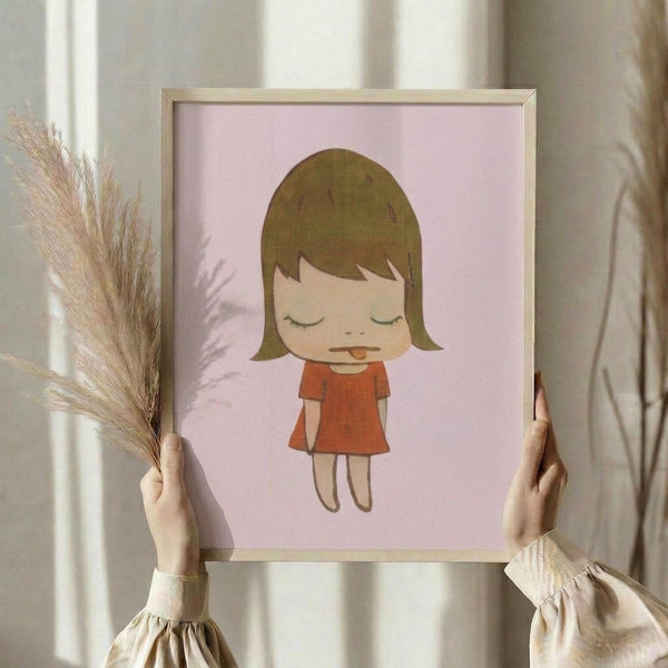 May include: Hands holding a framed art print featuring a minimalist illustration of a young girl with brown bob haircut, closed eyes, and red dress with her tongue sticking out, set against a soft pink background. The artwork is displayed in a simple wooden frame. Person wearing cream-colored ruffled sleeves holds dried wheat stalks in one hand while positioning the framed print against white curtains in soft natural lighting.
