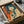 Vintage-style poster featuring a woman with blue bob haircut holding a revolver, rendered in retro orange and blue color scheme with Japanese text. The framed artwork is carefully packed in a cardboard box with protective tissue paper wrapping, shown during unboxing with wooden handles visible alongside.