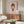 May include: Framed poster with pink background featuring cartoon-style illustration of young girl with brown bob haircut, red dress, and tongue sticking out, displayed above wooden mid-century credenza in modern living room with white curved chair, glass coffee table, and white table lamp