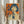 May include: Person holding framed vintage-style poster featuring Japanese woman with dark bob haircut holding Coca-Cola bottle against bright orange background with blue Japanese characters. Poster has light wood frame. Person wears cream ruffled sleeves and holds dried wheat stems, standing near white curtained window in soft natural lighting.
