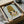 May include: Framed poster print featuring an anime-style illustration of a young girl with golden blonde hair and large dark eyes, wearing a yellow top against a pale mint green background. The artwork is displayed in a black frame, carefully packaged in brown cardboard boxes with white tissue paper wrapping. The minimalist cartoon character has a sweet, innocent expression with rosy cheeks and is rendered in soft, muted tones.