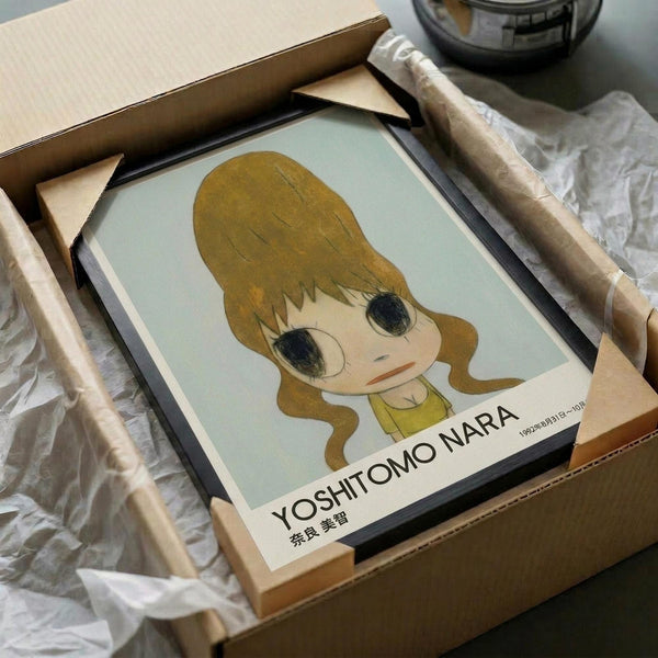 May include: Framed poster print featuring an anime-style illustration of a young girl with golden blonde hair and large dark eyes, wearing a yellow top against a pale mint green background. The artwork is displayed in a black frame, carefully packaged in brown cardboard boxes with white tissue paper wrapping. The minimalist cartoon character has a sweet, innocent expression with rosy cheeks and is rendered in soft, muted tones.