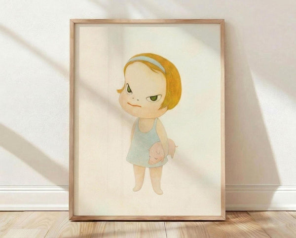 May include: Framed art print featuring a cute illustrated character with blonde bob haircut, green eyes, and light blue dress, displayed in light wood frame against white textured wall on wooden floor with soft natural lighting casting shadows.